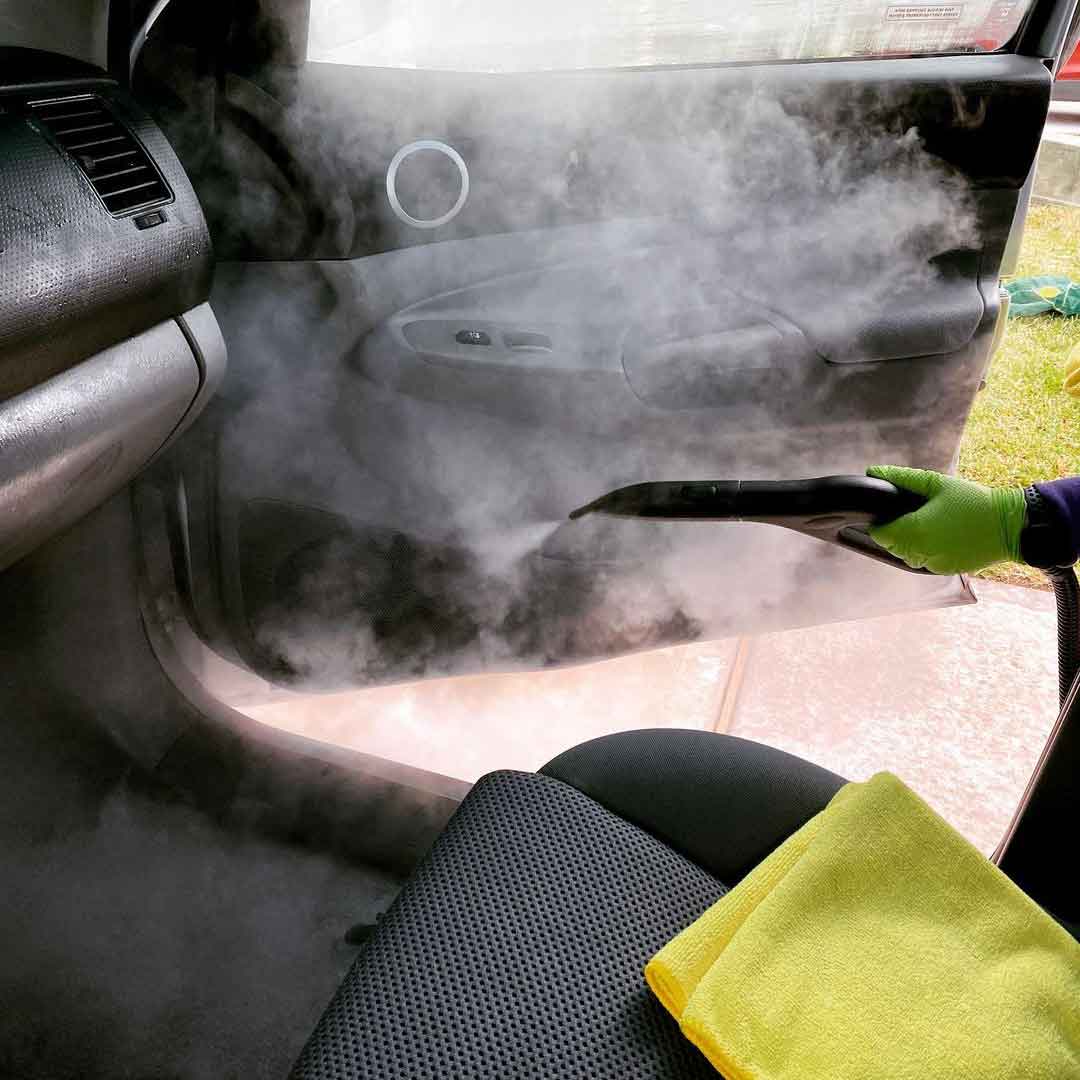 Aqua Pro Steamer with a jet nozzle attachment producing steam to clean a car door panel during an auto detailing session.