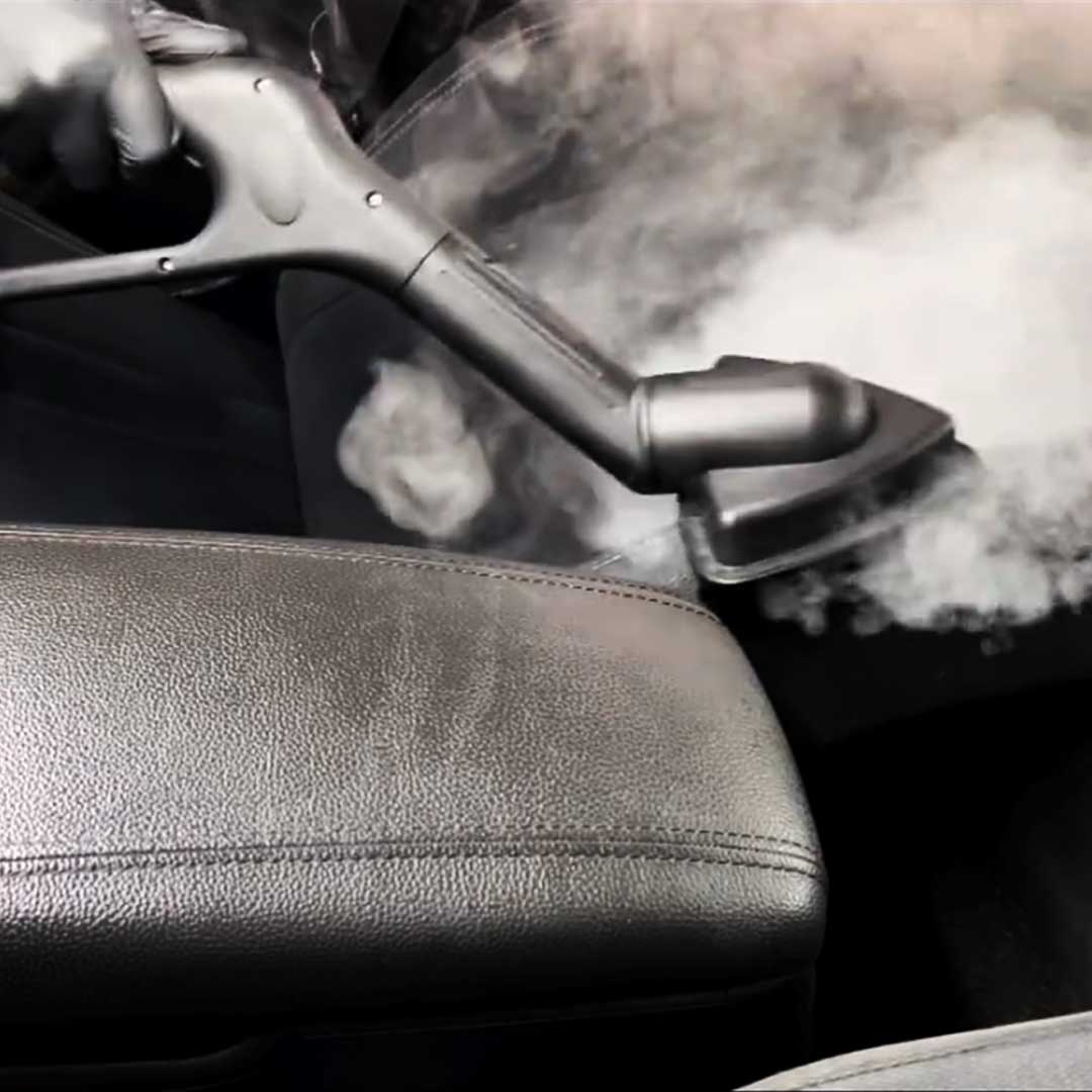 Close-up of Aqua Pro Steamer with a triangle brush attachment emitting steam to clean a leather car seat and armrest.