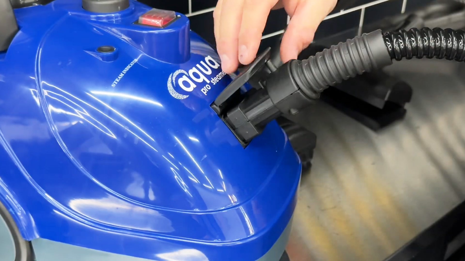 Close-up of the Aqua Pro Steamer with a hand attaching a black hose to the steam cleaner, showing the device being set up for use.